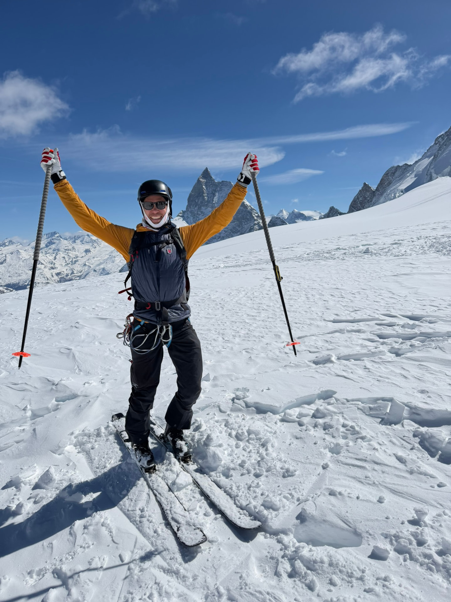 Andreas Wadström på skidor på en glaciär med armarna i luften och spetsiga toppar bakom
